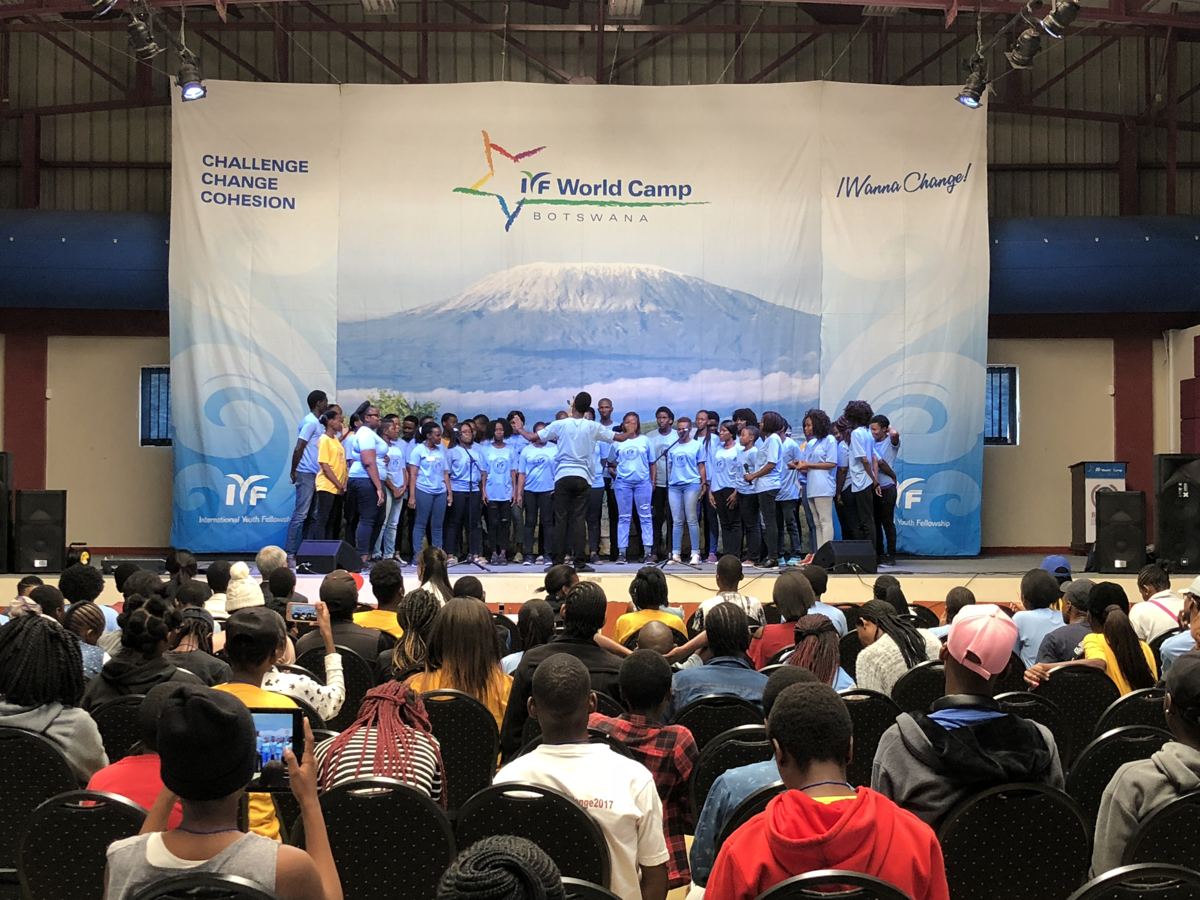 A choir in light blue shirts singing on stage in front of a full hall.
